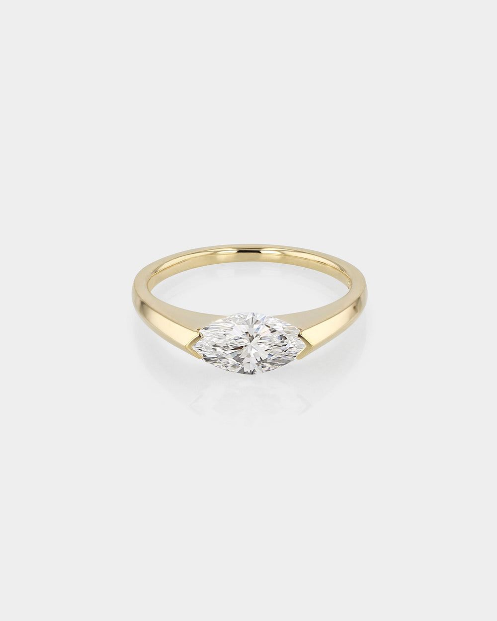 18k yellow gold solitaire engagement ring featuring an East-West oriented marquise cut diamond set in a polished half-bezel. The ring showcases a wide, solid band design and a flush-set center stone with an open back.