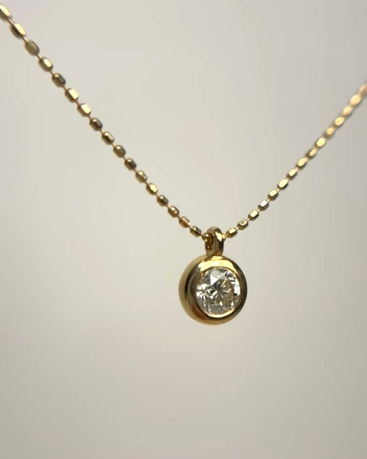 18k yellow gold necklace featuring a 1ct round brilliant cut diamond in a circular bezel setting. The solitaire pendant hangs from a delicate gold chain.